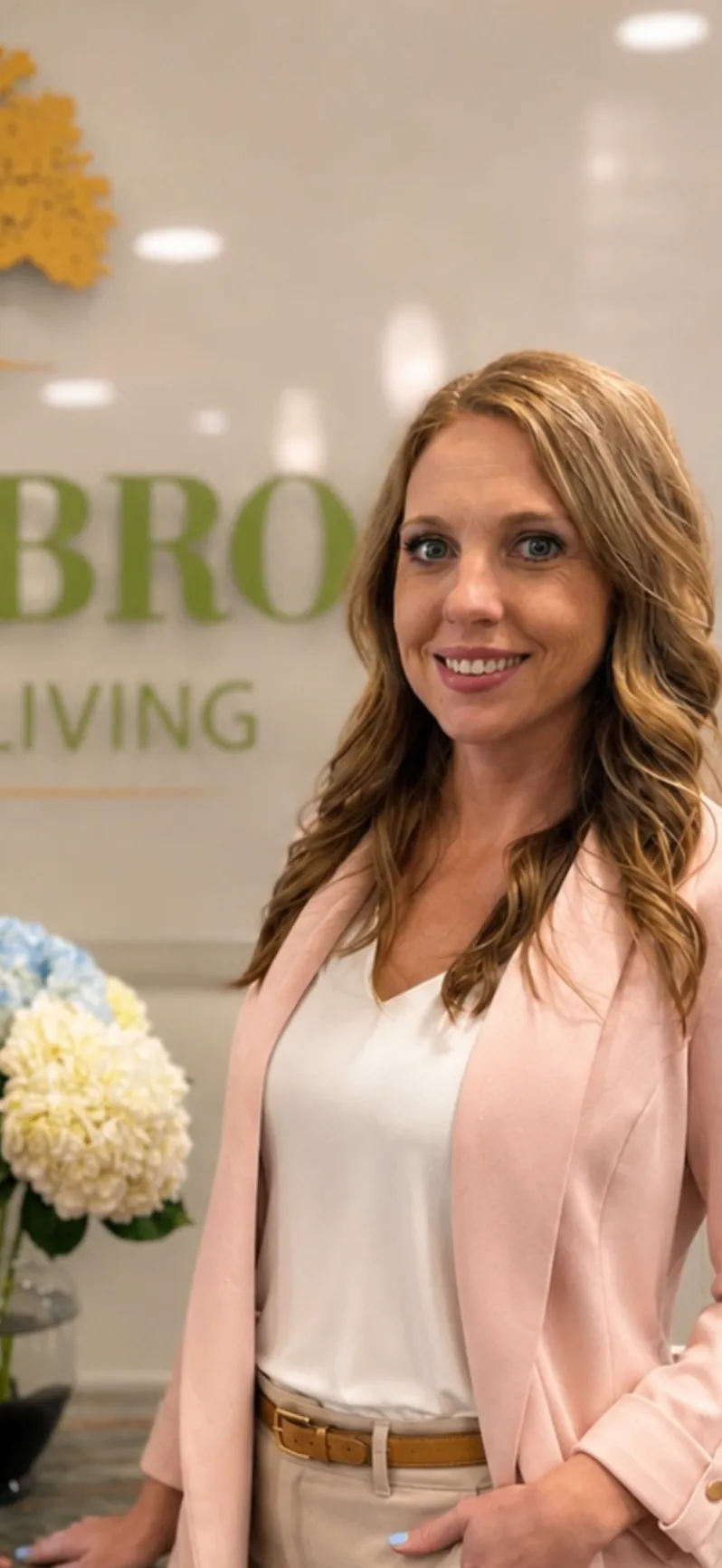 Sarah Martin smiling in a pink blazer inside Saddlebrook Senior Living