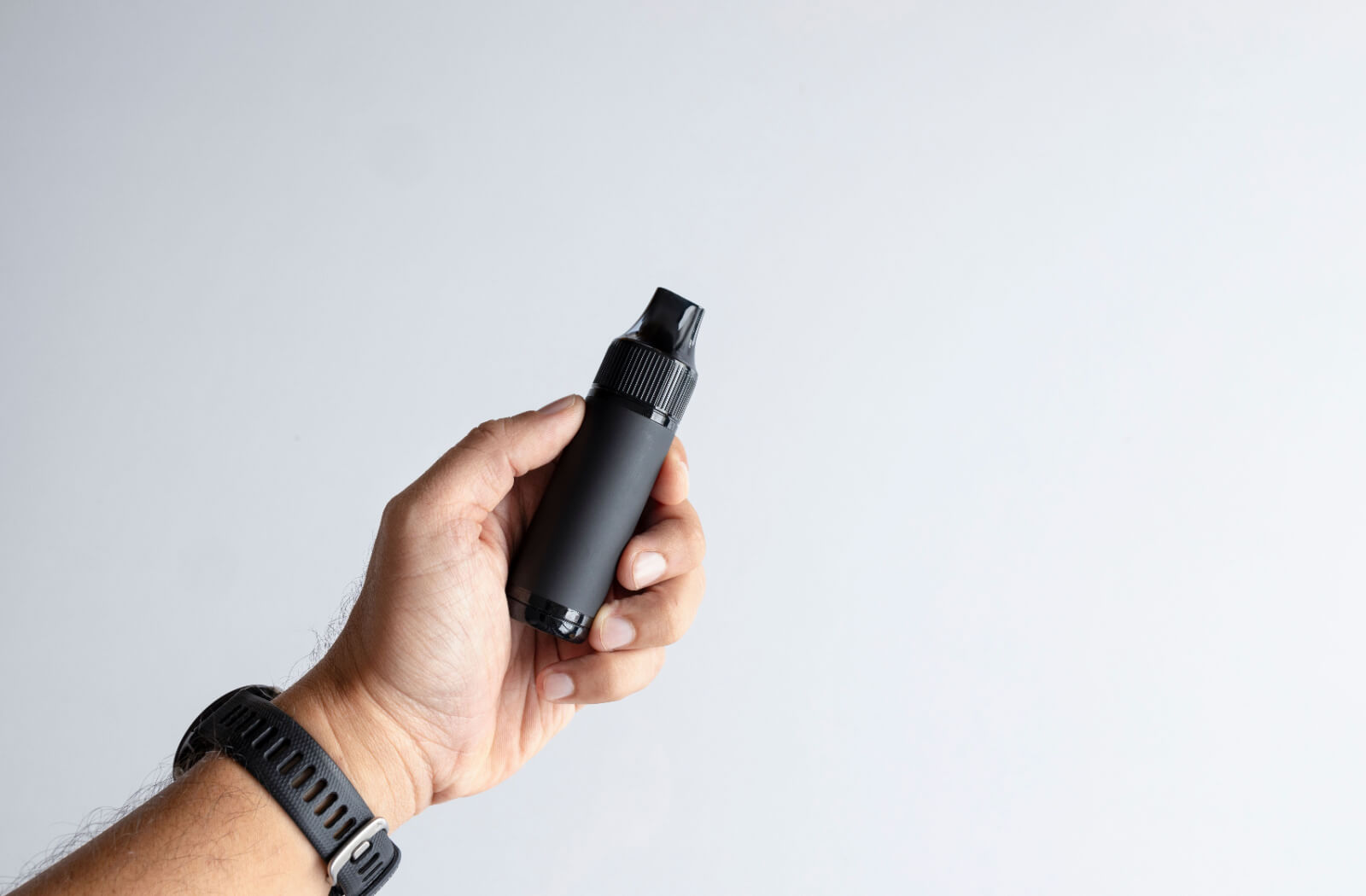 A close-up image of a hand holding a black vaping device in front of a gray background.